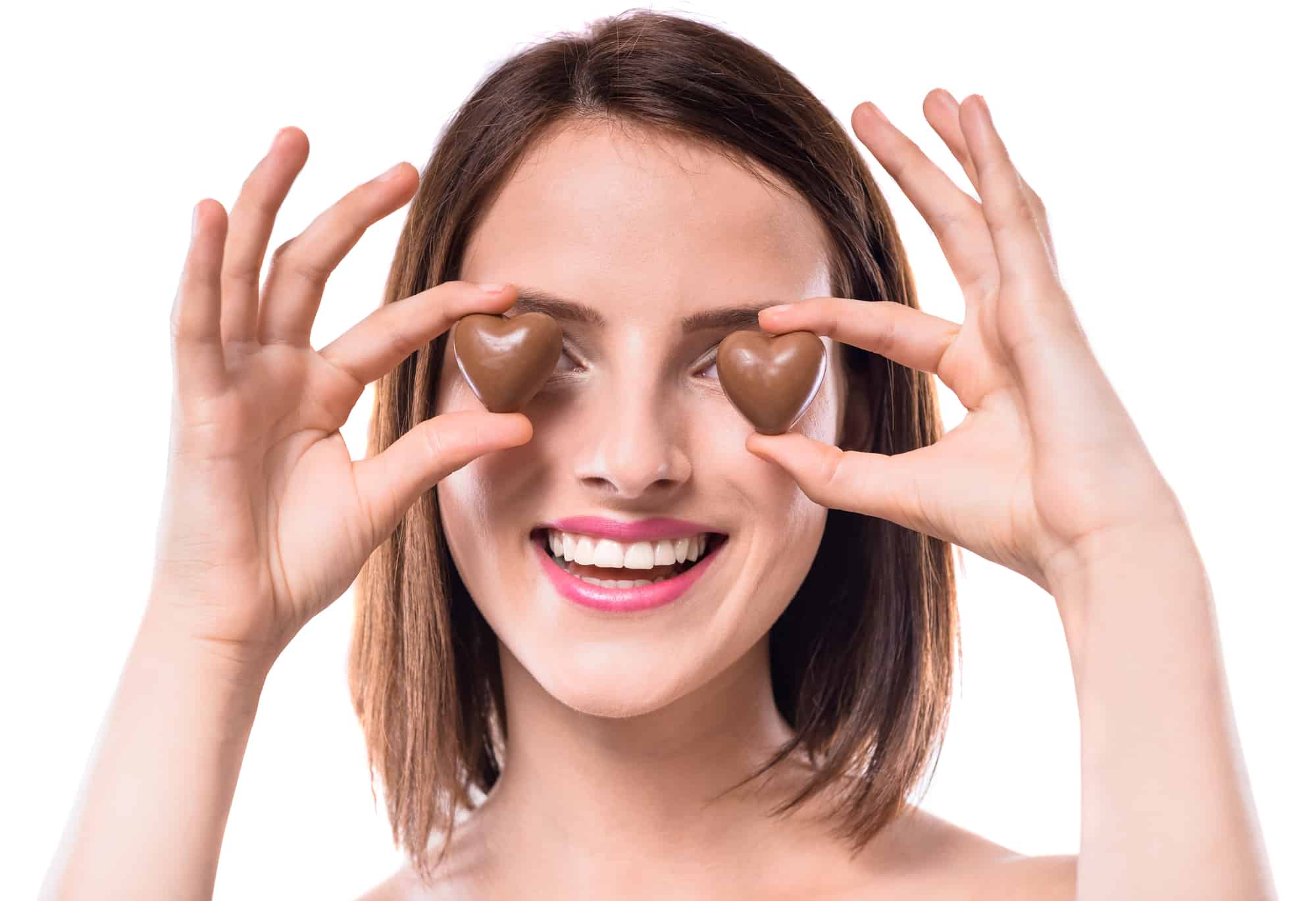 Sweet temptation. Beautiful woman holding heart-shaped chocolate candies over white background.